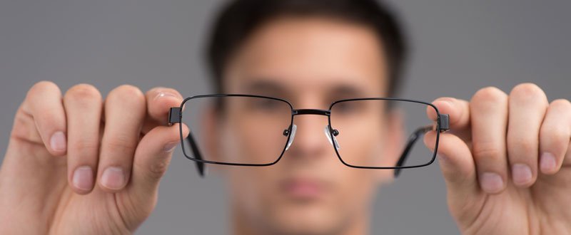 A man with blurred vision holding his glasses