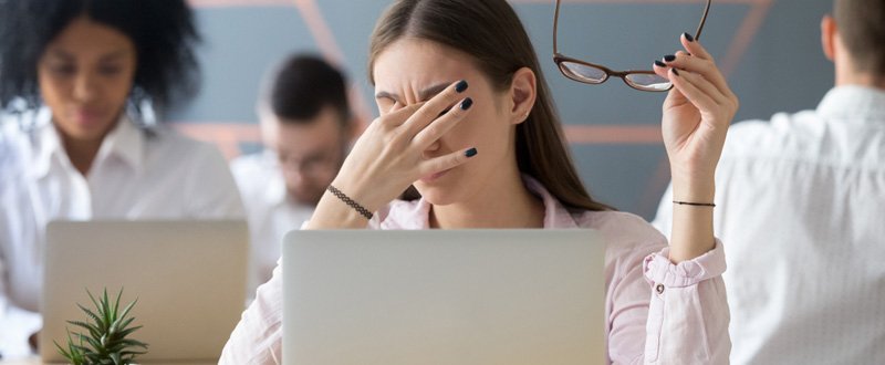 A young woman rubbing her tired eyes due to computer use