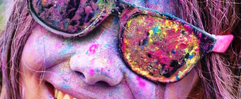 A young woman wearing goggles and playing holi